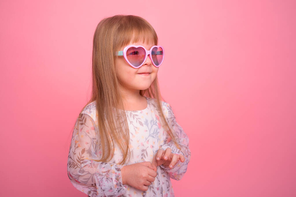 портрет милой маленькой девочки в розовых солнечных очках на розовом фоне - Фото, изображение