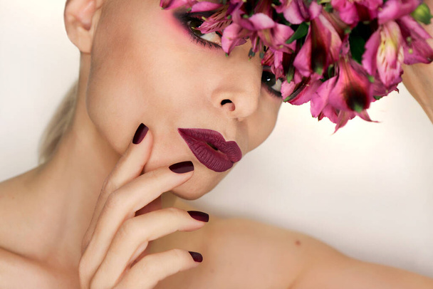 Burgundy manicure and makeup on a girl with flowers. - Фото, изображение