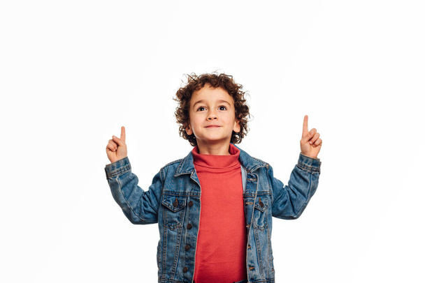 Young boy pointing up to show something while standing on an isolated white background. - Foto, afbeelding