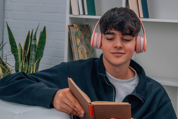 молодий чоловік вдома читає книгу і слухає музику з навушниками
 - Фото, зображення