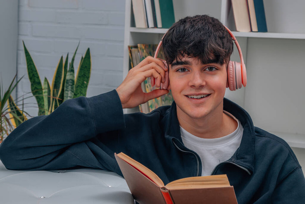 Młody człowiek w domu czyta książki i słucha muzyki ze słuchawkami - Zdjęcie, obraz