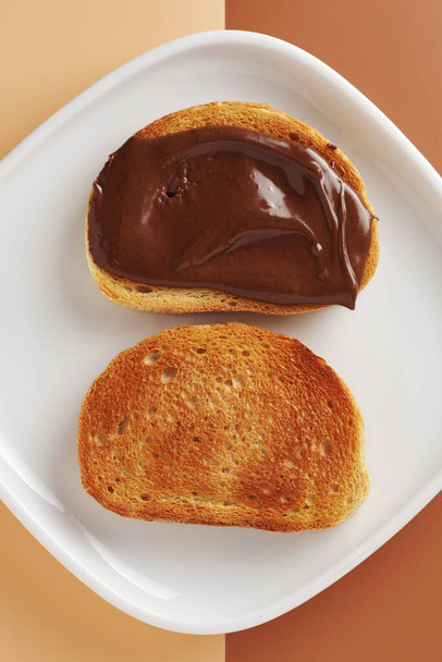 Brood met gespreide chocoladepasta op een bord met twee kleuren achtergrond, bovenaanzicht - Foto, afbeelding