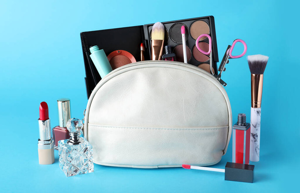 Bolso cosmético y productos de maquillaje con accesorios sobre fondo azul claro - Foto, imagen