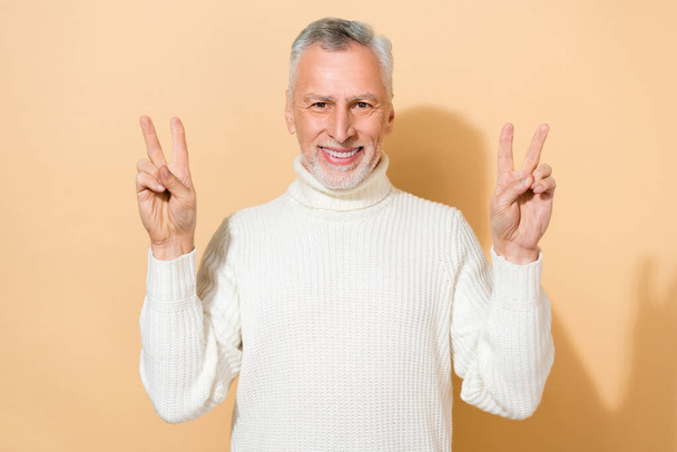 Portrait of attractive cheerful grey-haired man showing double v-sign good mood isolated over beige pastel color background - Photo, image
