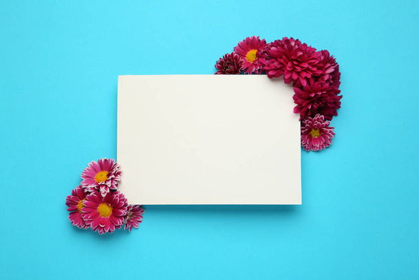 Beautiful chrysanthemum flowers and blank card on light blue background, flat lay. Space for text - Valokuva, kuva