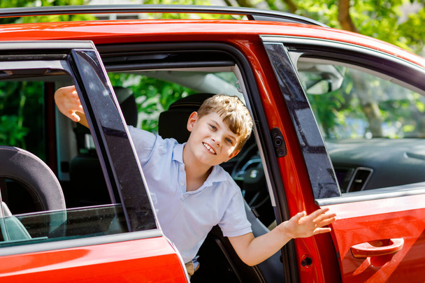 Happy child, school boy sitting in car before leaving for summer vacation with parents. Happy kid by window of car going on journey, family road trip - Foto, imagen