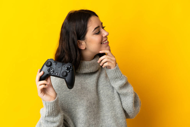 Frau spielt mit einem Videospielcontroller auf gelbem Hintergrund, denkt eine Idee nach und schaut zur Seite - Foto, Bild
