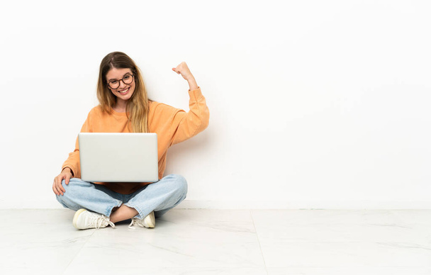 Młoda kobieta z laptopem siedząca na podłodze i wykonująca silny gest - Zdjęcie, obraz