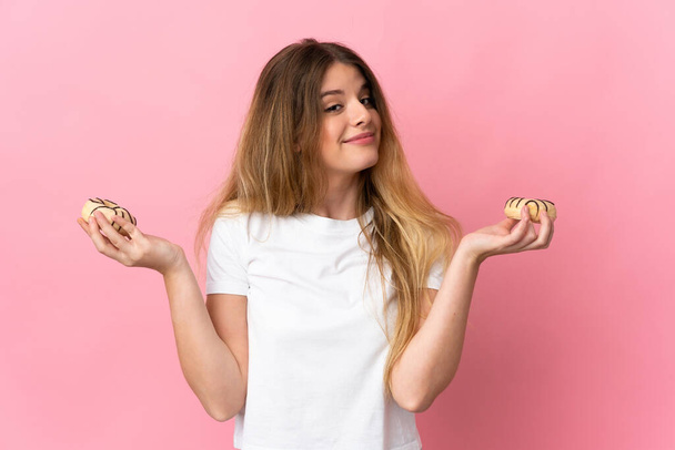 Young blonde woman isolated on pink background holding donuts - Foto, afbeelding