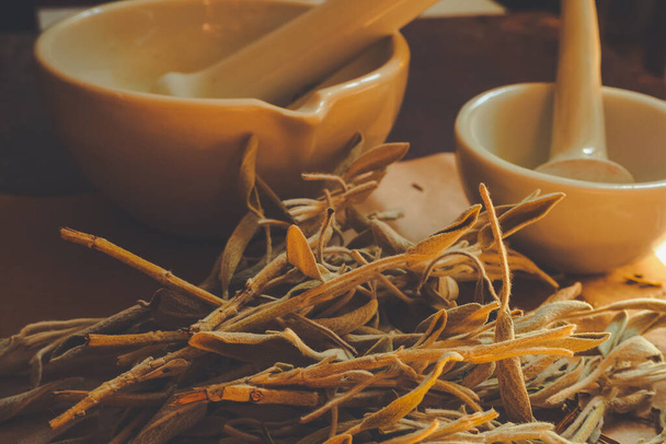 Sementes de cânhamo triturado e ervas de sálvia secas em uma superfície de mesa áspera com uma argamassa de cerâmica branca velha e pilão - Foto, Imagem