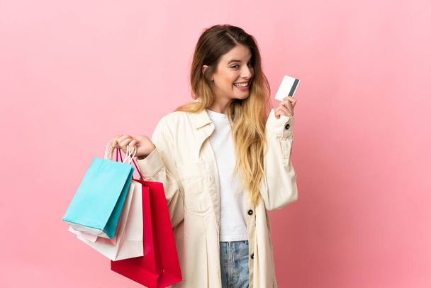 Young woman with shopping bag isolated on pink background holding shopping bags and a credit card - Фото, зображення