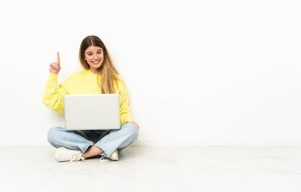 Giovane donna con un computer portatile seduto sul pavimento che indica una grande idea - Foto, immagini