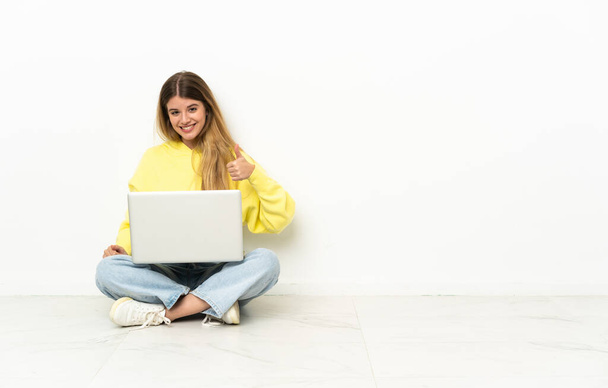 Молодая женщина с ноутбуком, сидящая на полу и показывающая большой палец вверх. - Фото, изображение