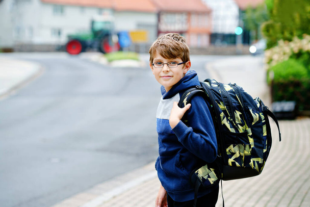 Χαρούμενο αγοράκι με τσάντα και γυαλιά. Ένα σχολιαρόπαιδο που φορούσε γυαλιά στο δρόμο για το γυμνάσιο. Ενθουσιασμένο παιδί στην αυλή του σχολείου. Πίσω στο σχολείο.. - Φωτογραφία, εικόνα