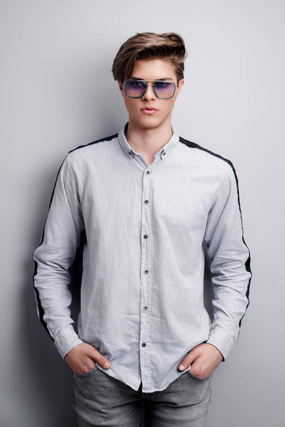 handsome guy standing in stylish sunglasses holds arms in pockets, isolated on a gray background - Foto, immagini