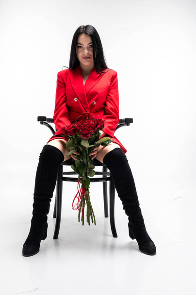 Beautiful brunette in red jacket holding a bouquet of red roses. Valentine's Day and International Women's Day, March 8 celebration. White Background - Φωτογραφία, εικόνα