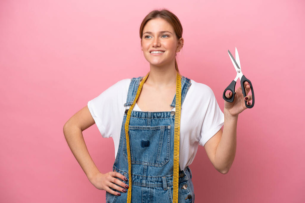 Young caucasian seamstress woman isolated on pink background posing with arms at hip and smiling - Photo, Image