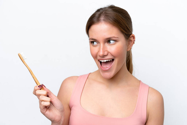 Young caucasian woman isolated on white background with a toothbrush and surprised expression - Фото, зображення