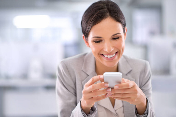 Siempre está disponible. Fotografía de una mujer usando un teléfono celular mientras está sentada en un escritorio en una oficina. - Foto, Imagen