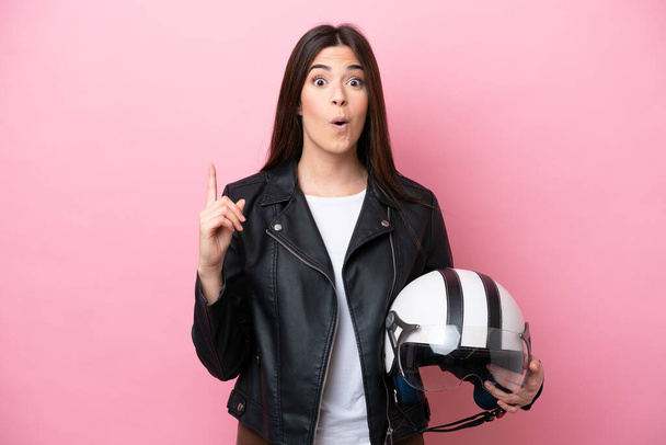 Mujer brasileña joven con casco de moto aislado sobre fondo rosa con la intención de realizar la solución mientras levanta un dedo - Foto, Imagen
