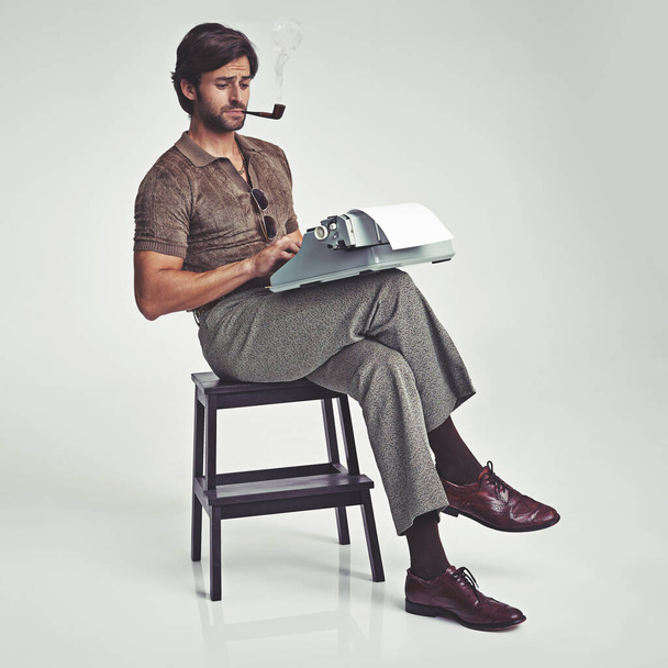 Who needs a desk anyway. Studio shot of a 70s style businessman sitting on a stool using a typewriter. - Фото, зображення