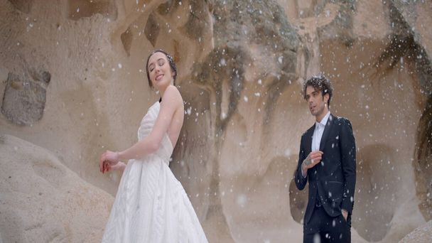 Photo shoot of the newlyweds in nature. Action. A cute couple in wedding costumes in the mountains posing for a photo session and its snowing. - Foto, Imagen