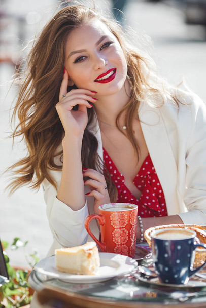 Beautiful young woman outdoor. Attractive young lady sitting at cafeteria drinking coffee. - Photo, Image