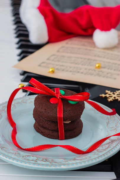 Christmas cookies heap, music sheet and santa's red hat on piano. - Foto, imagen