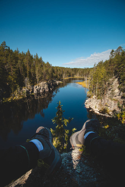 podróżnik siedzi na wysokiej skale i obserwuje piękne naturalne jezioro w hiidenportti parku narodowym, Sotkamo w regionie kainuu, Finlandia. Wędrówki po fińskiej wsi. - Zdjęcie, obraz