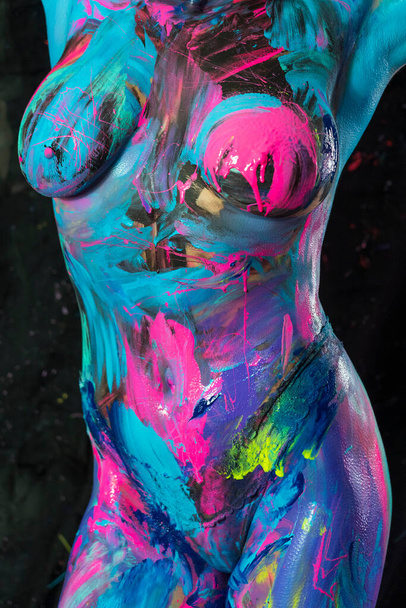 A gorgeous female model is painted with vibrant colors on her skin as a canvas in a studio environment - Photo, image