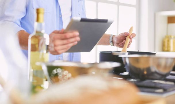 Hombre siguiendo la receta en la tableta digital y cocinar comida sabrosa y saludable en la cocina en casa - Foto, Imagen