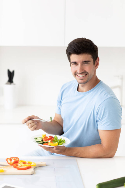 Lifestyle, health and nutrition. Handsome young man eating healthy food during lunch break with plate enjoying vegetables. - Фото, изображение