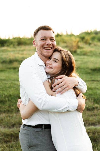 happy guy hugs his bride at sunset of the day. portrait of a couple in love. happy young people of european appearance. summer honeymoon day - Foto, immagini