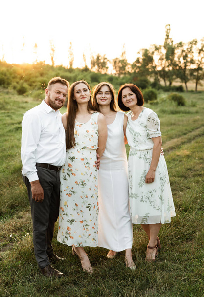 father and mother of middle age tenderly hug two adult daughters in nature. beautiful family walks across the field at sunset of the day. parents with older children - Fotografie, Obrázek