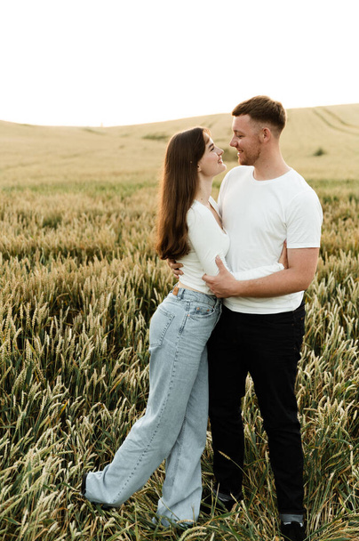 young couple in love stand in a wheat field at sunset of the day. guy with a girl on a romantic summer date. cute couple of lovers - Foto, imagen