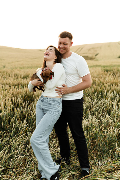 portrait of a young couple with a pet. the guy hugs the girl holding the dog. people in love walking along the field with a dog.lovers with a dog - Фото, зображення