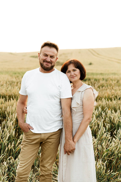 portrait of a middle-aged couple in nature. husband and wife are smiling cute while in the field on the back of the day - Foto, imagen
