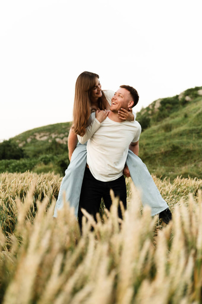 cute girl on the back of her boyfriend. beautiful couple have fun in nature. guy with a girl in a wheat field. man and woman laughing - Fotoğraf, Görsel