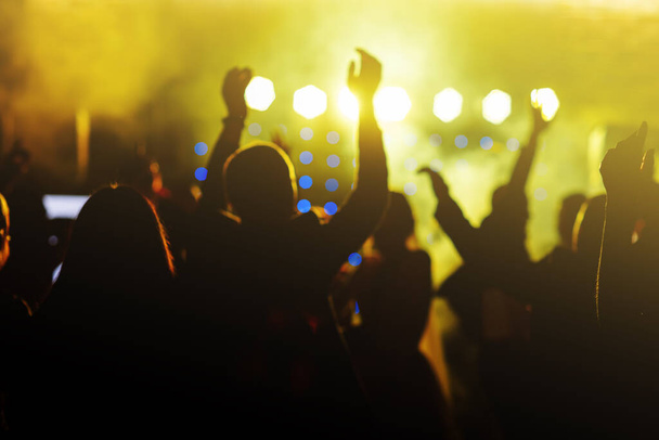 明るい黄色の舞台照明の前で群衆を応援します。ディスコナイトクラブや音楽祭のコンサートで人々が踊るシルエットのイメージ - 写真・画像