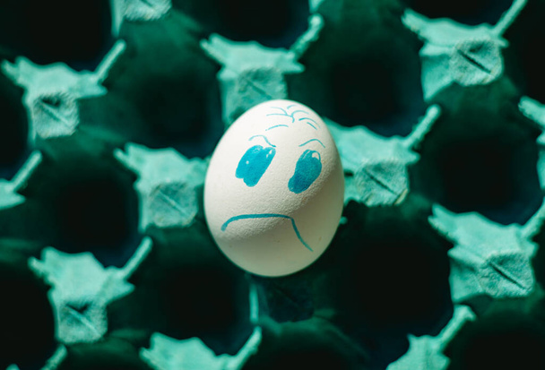 Cara enojada huevo de gallina blanca en una bandeja. Fotografía de cerca. Concepto de emociones y dificultades de la vida. - Foto, Imagen