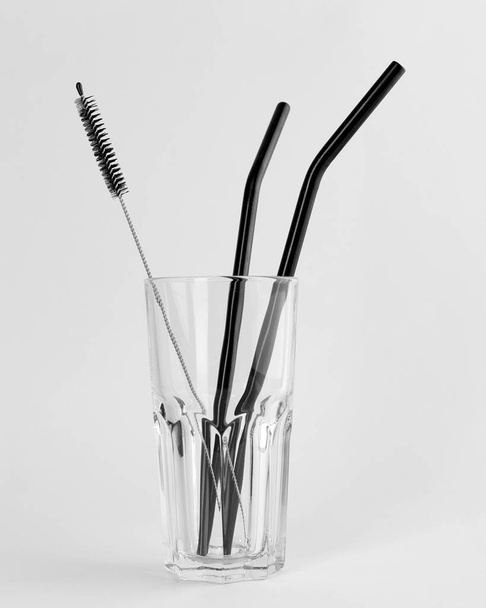 Reusable metal straws for drinks and a small brush in a glass cup. Isolated on white background - Foto, afbeelding