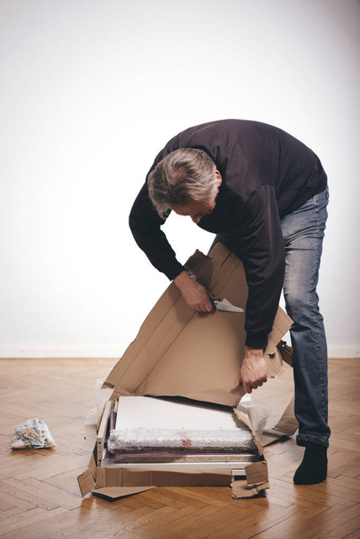 Man unpacking paper box with set of three laminated wood drawers  - Foto, afbeelding