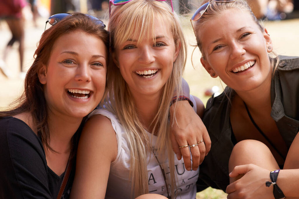 Traîner avec les filles. Portrait de trois amis souriants assis bras dans le bras et lors d'un festival. - Photo, image