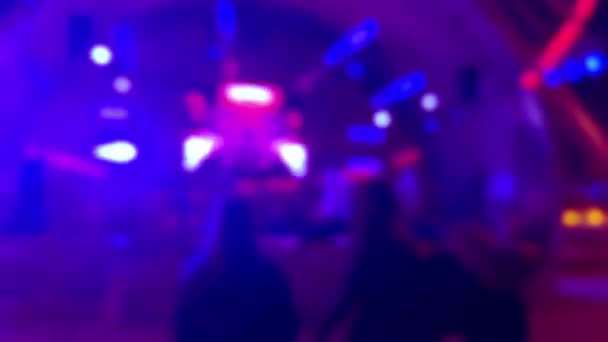 Siluetas de tres chicas bailando cerca de un escenario en un club nocturno: fondo borroso.  - Metraje, vídeo