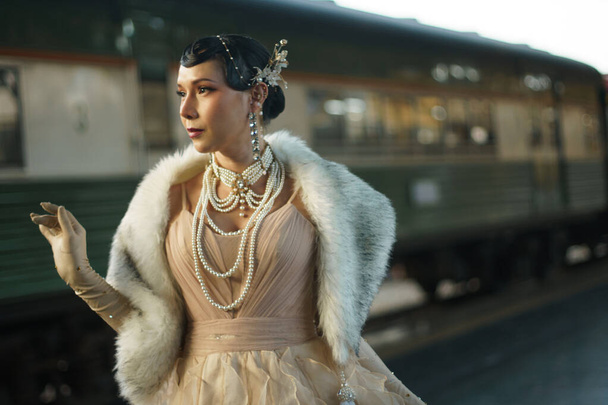 Retro vintage portrait of beautiful Gatsby woman stand look around, wait coming train for lover, feeling expression face romantic 20s fashion style at public train station, Gatsby old fashion concept - Photo, Image