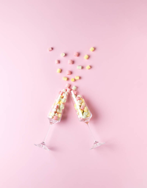 Twee grote glazen glazen met veelkleurige marshmallows op een roze achtergrond. Het concept van Valentijnsdag. Vlakke plaat. - Foto, afbeelding
