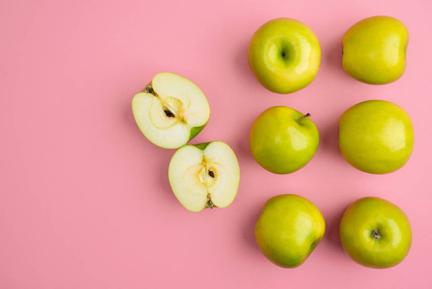 Πράσινα μήλα ολόκληρα και κομμένα κοντά σε ανοιχτό ροζ φόντο με χώρο αντίγραφο για το κείμενο, επίπεδη lay. Απρόσκοπτη μοτίβο από πράσινα μήλα σε ροζ φόντο - Φωτογραφία, εικόνα