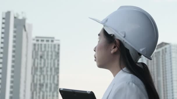 İnşaat alanında tablet bilgisayarı olan kadın inşaat mühendisi. Beyaz kasklı, kendine güvenen bir mimar inşaat alanına bakıyor. İnşaat ve mimari kavramı. - Video, Çekim
