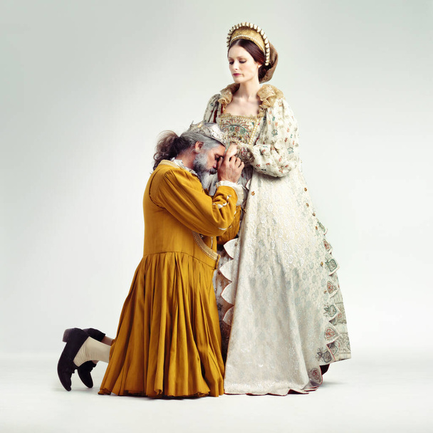 Een koninklijke belofte. Studio shot van een koning knielen en kussen zijn koninginnen hand. - Foto, afbeelding