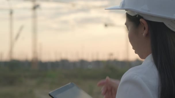 Gün batımında inşaat alanında tablet bilgisayarlı kadın inşaat mühendisi. Beyaz kasklı, kendine güvenen bir mimar inşaat alanına bakıyor.. - Video, Çekim